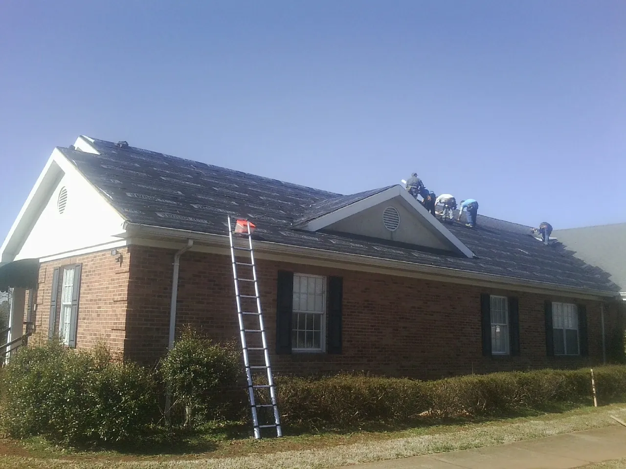 Crew tearing shingles off a brick ranch roof with a ladder set — Metal Roof Repair work by our crew in Hutchinson