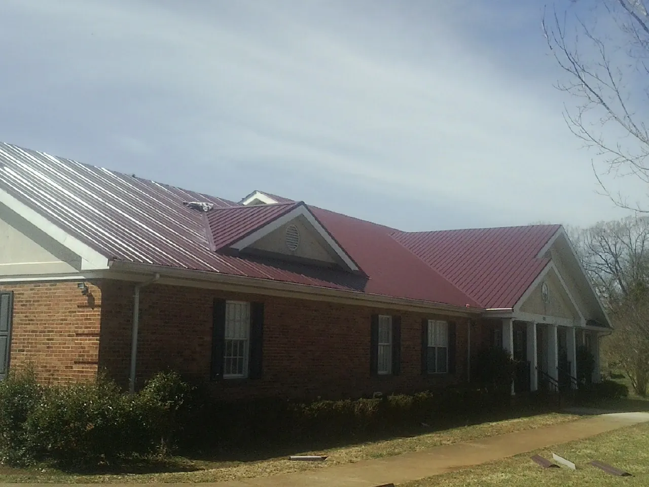 Red metal roof with gabled entries on a long brick building, from a Hail Damage Roof Repair job in Hutchinson
