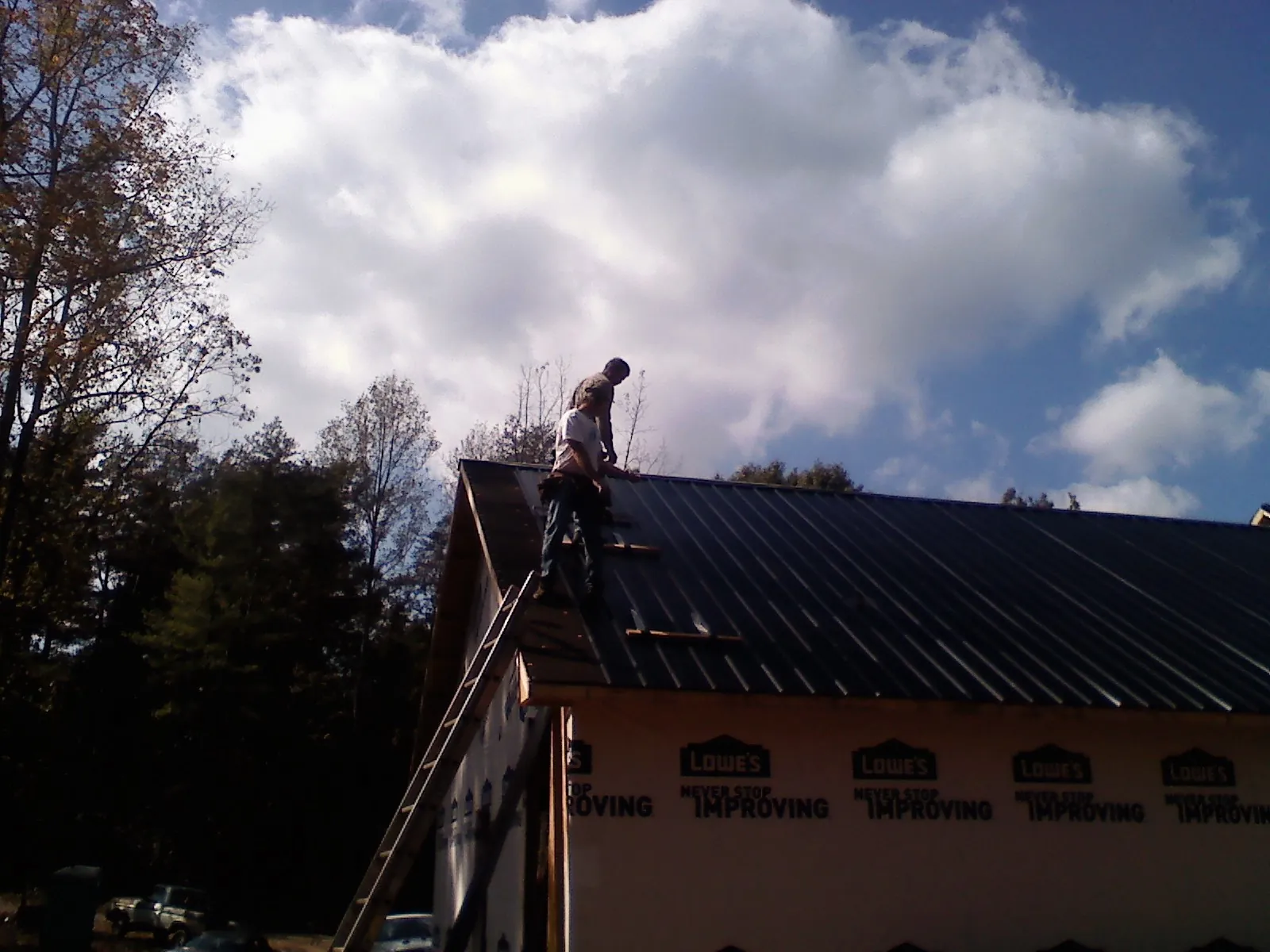 Roofer fastening dark metal panels high against a cloudy sky, from a Roof Inspection job in Hutchinson