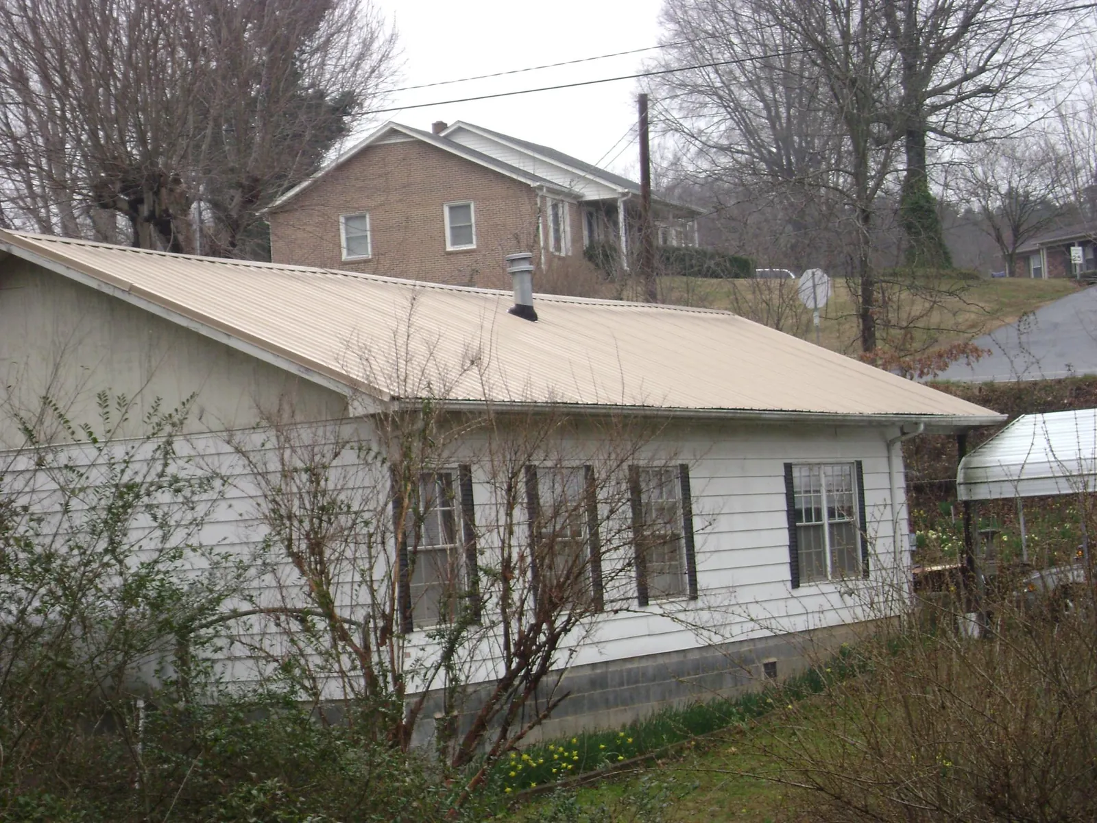 Tan metal roof on a white sided house set into a hillside — Commercial Roofing by Roofing Brothers in Hutchinson